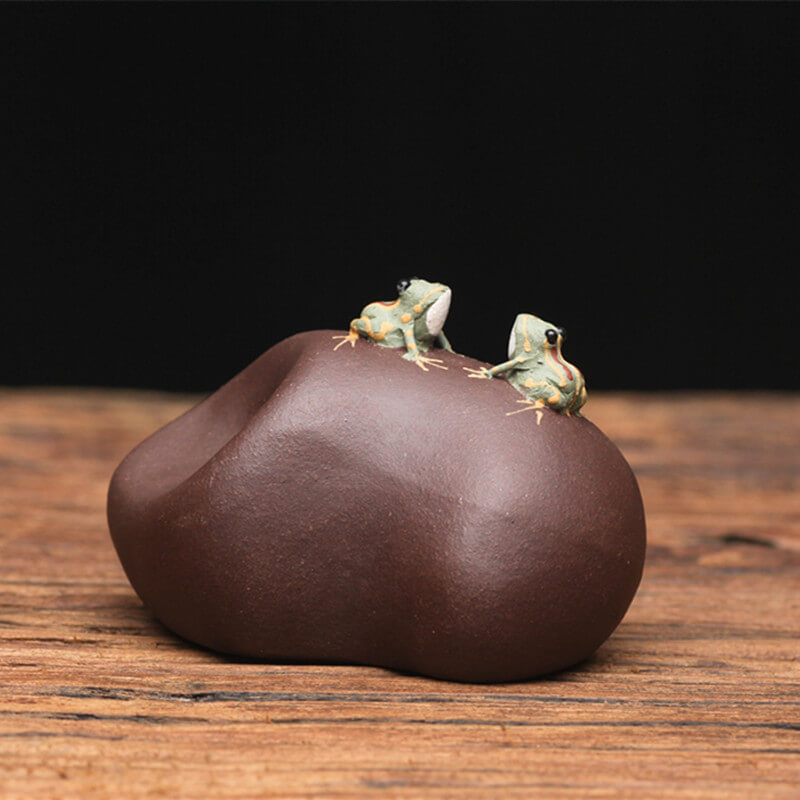 Chinese Spitting Tea Pet frogs figurines on a brown stone-like object with a dark background
