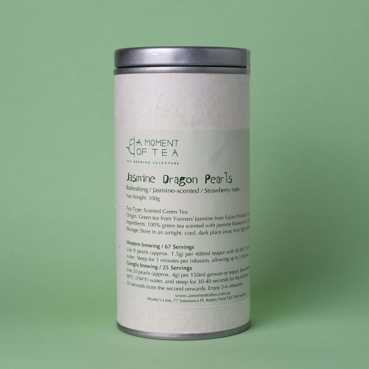 A tin container of Jasmine Dragon Pearls tea with some pearls displayed in front and a small glass bowl with pearls inside. The background is green.