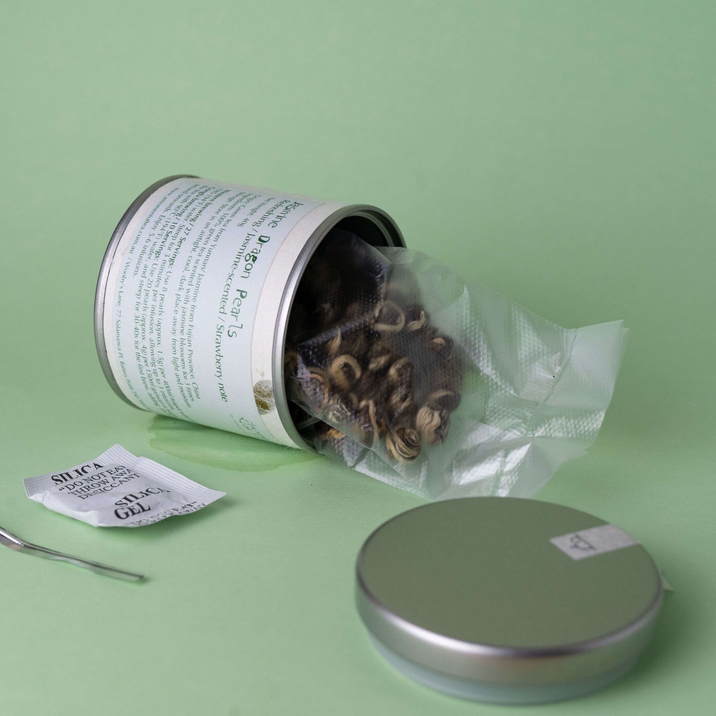 Open tin can with Jasmine Dragon Pearls green tea on a green background