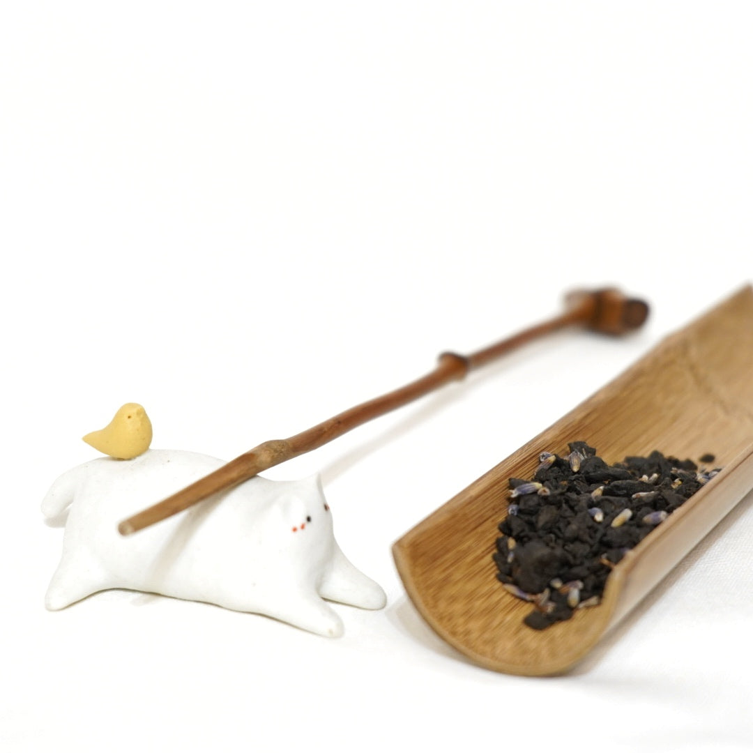 award winning lavender puerh tea presented on a wooden tray, including a small amount of loose tea and a teapot spoon, with a white background.