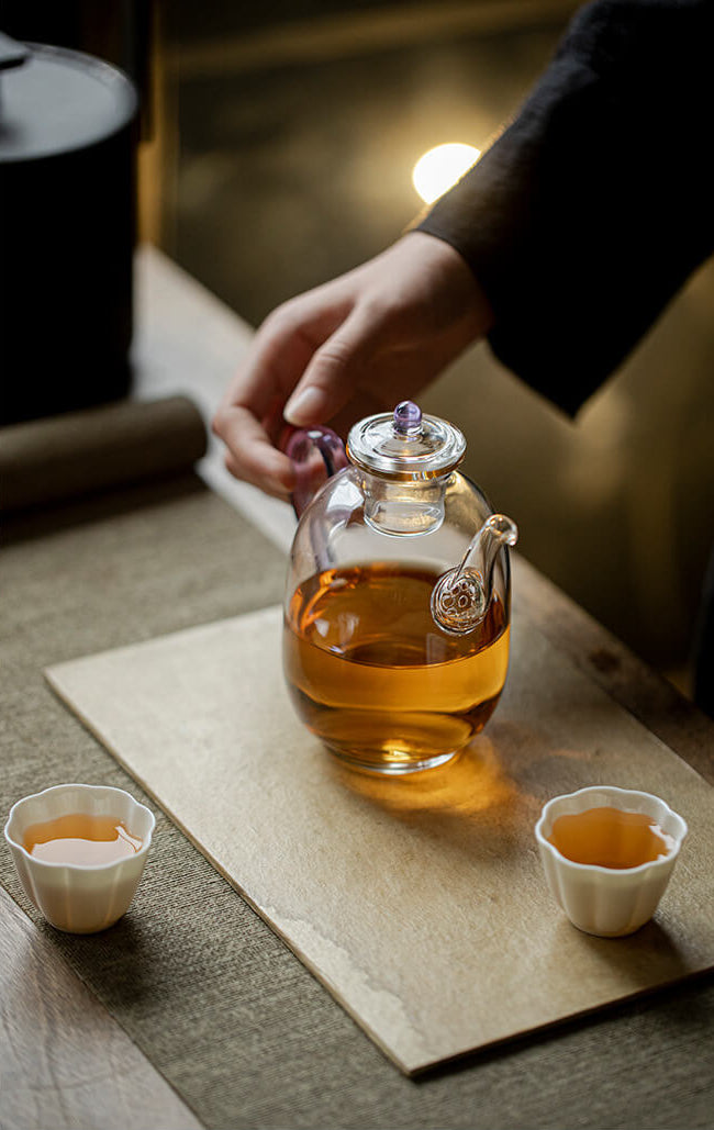 Tea ceremony setup with a glass teapot and cups on a wooden surface.