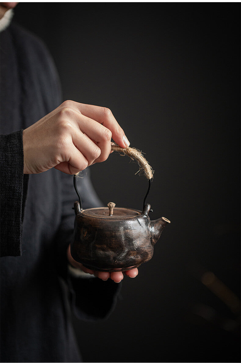Person holding a small black teapot with a dark background