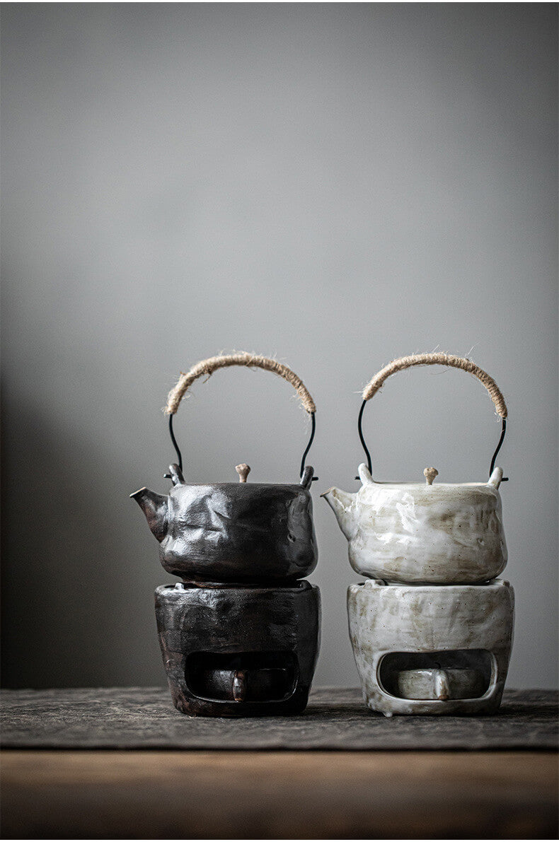 Two ceramic teapots with warmer on stands against a gray background