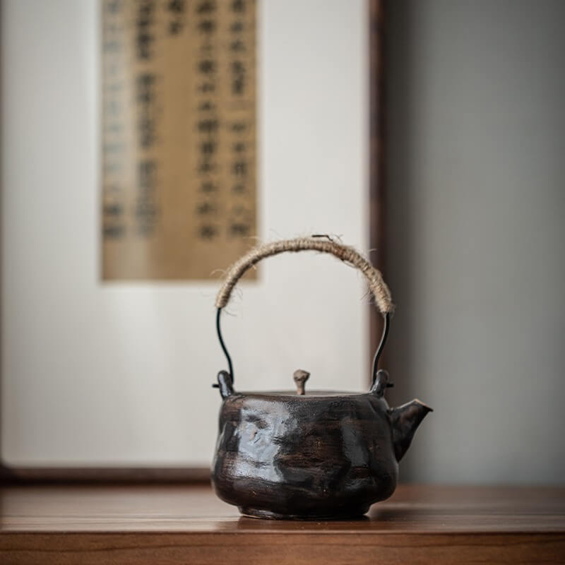Traditional ceramic teapot with a woven handle on a wooden surface, with a blurred background.
