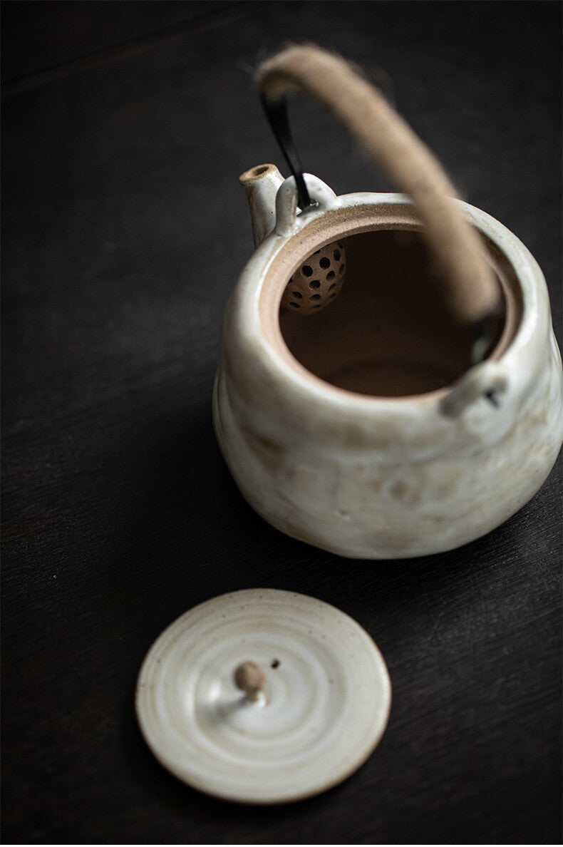 White ceramic teapot with a wooden handle on a dark surface