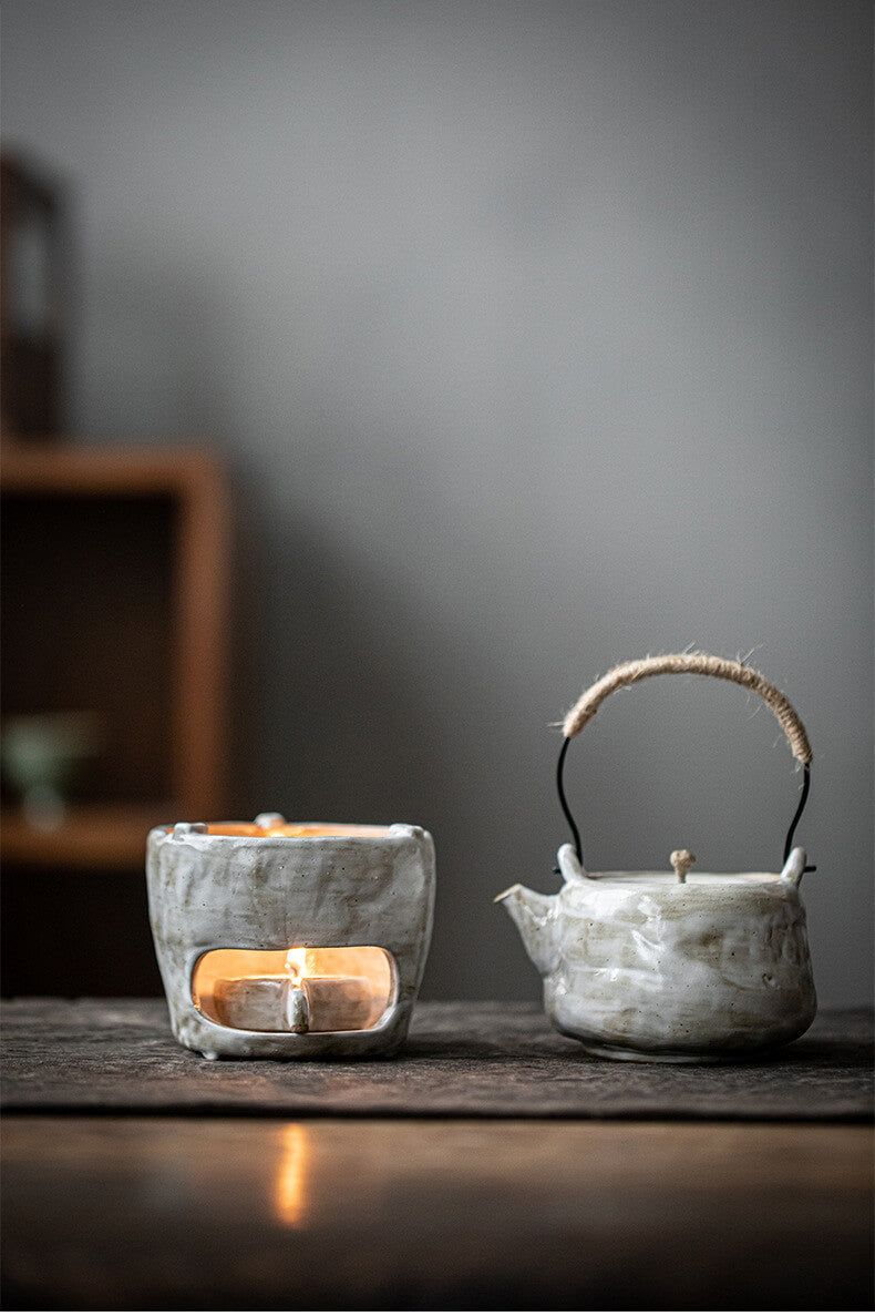 Teapot and warmer with candle on a wooden surface with a blurred background