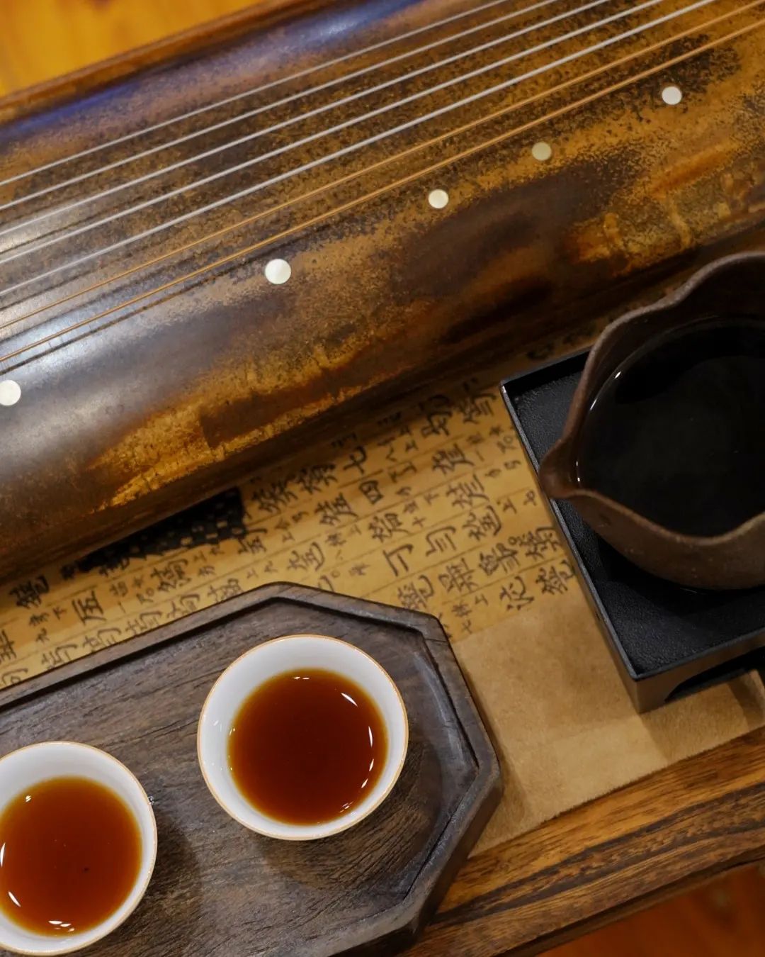 Two cups of dark amber pu-erh tea beside a guqin and calligraphy at A Moment of Tea in Hobart