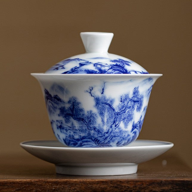 Blue and white gaiwan painted with a mountain landscape, on a dark wooden table