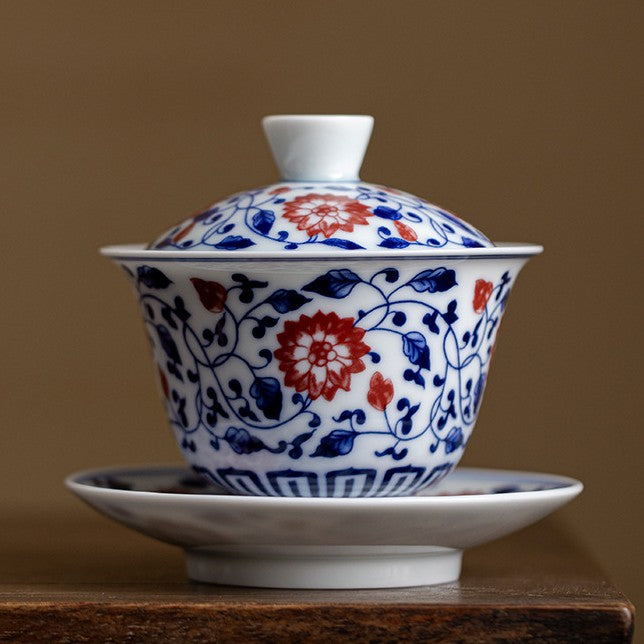 Blue and white gaiwan with interlocking lotus vine and underglaze red flowers, on a wooden table