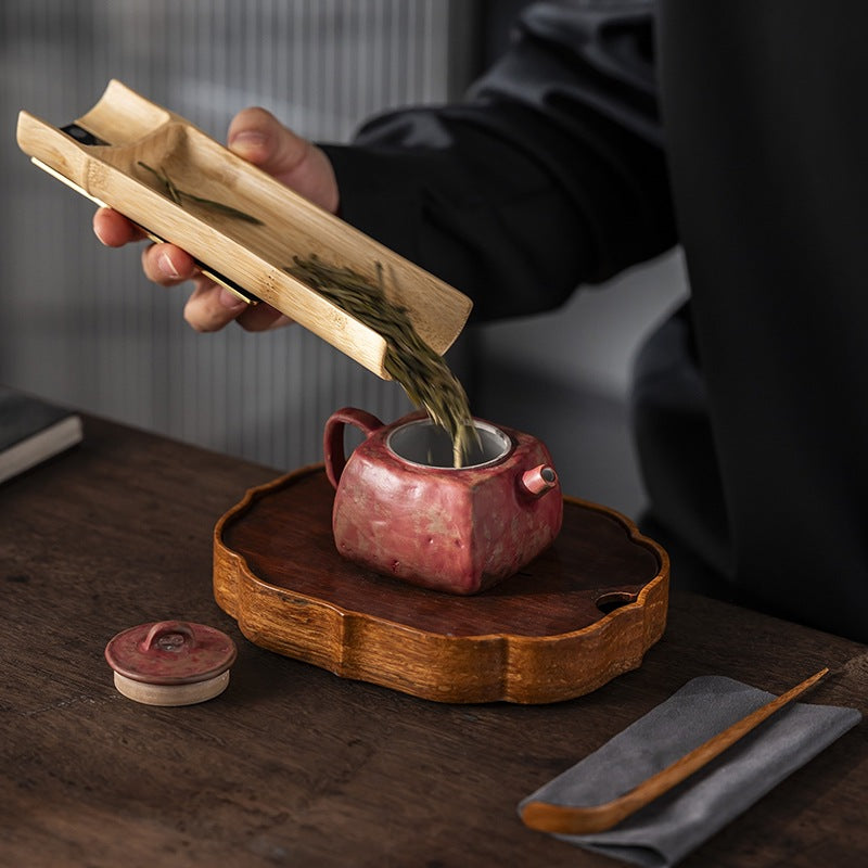 Tea leaf sliding from the bamboo tea scale into a red clay teapot