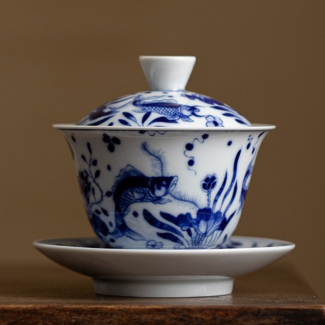 Blue and white gaiwan with fish and waterweed pattern, on a dark wooden table