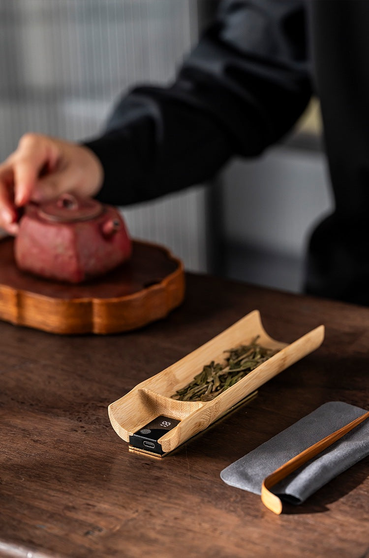 Bamboo tea scale on a tea table beside a clay teapot, USB charging port visible on the end panel