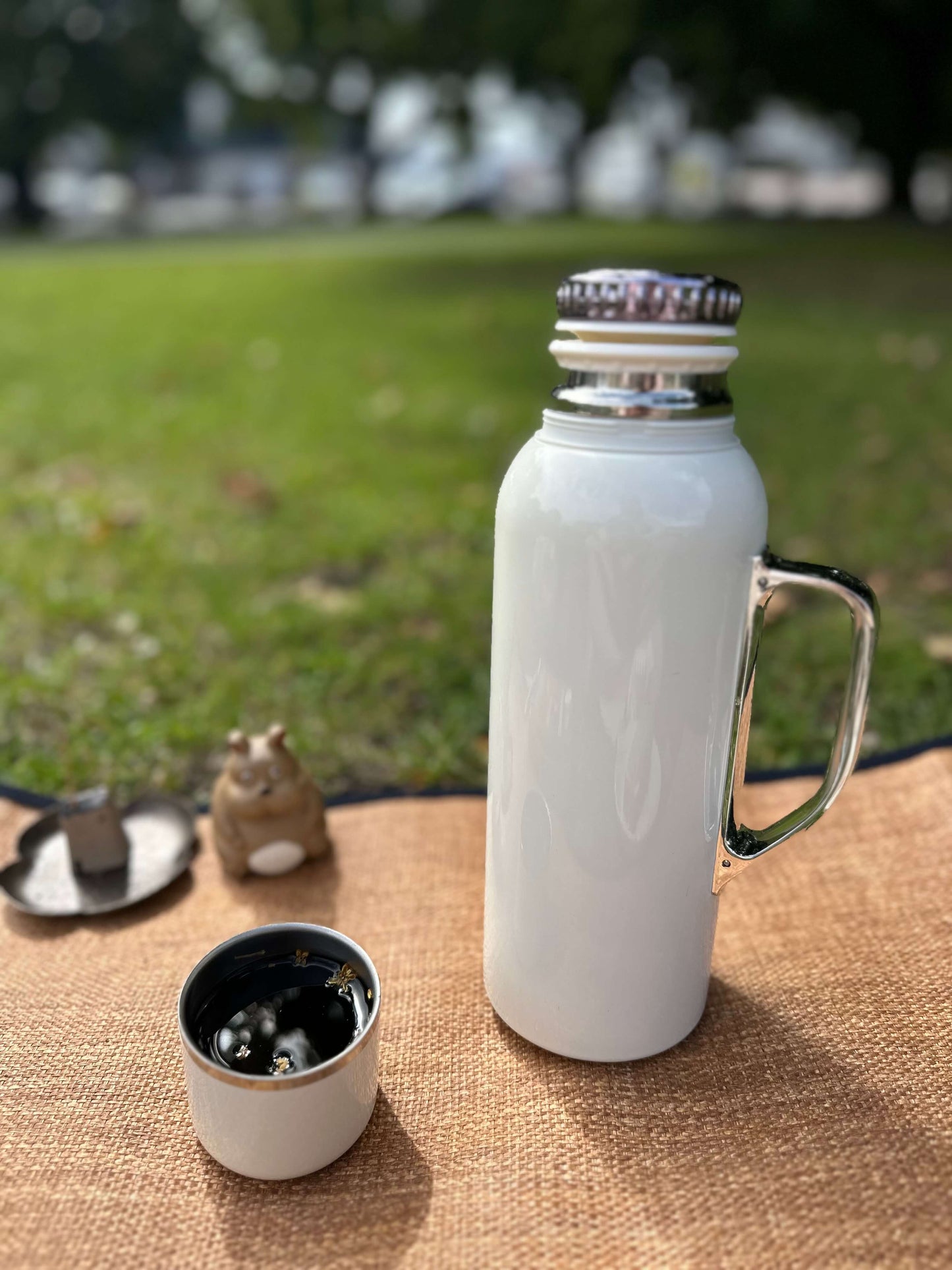 White insulated tea flask with handle on a woven mat outdoors