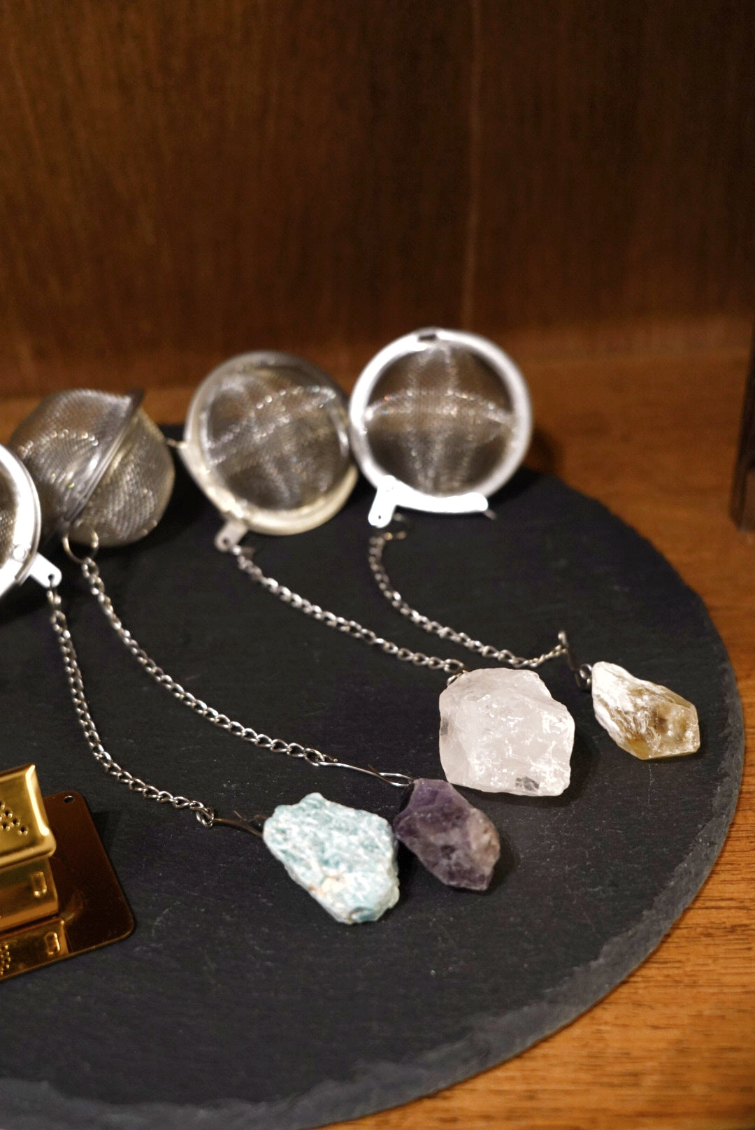 Four mesh tea infuser balls with raw amazonite, amethyst, clear quartz and smoky quartz stones on a slate board
