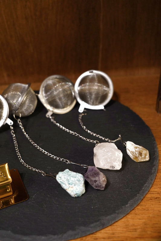 Four mesh tea infuser balls with raw amazonite, amethyst, clear quartz and smoky quartz stones on a slate board