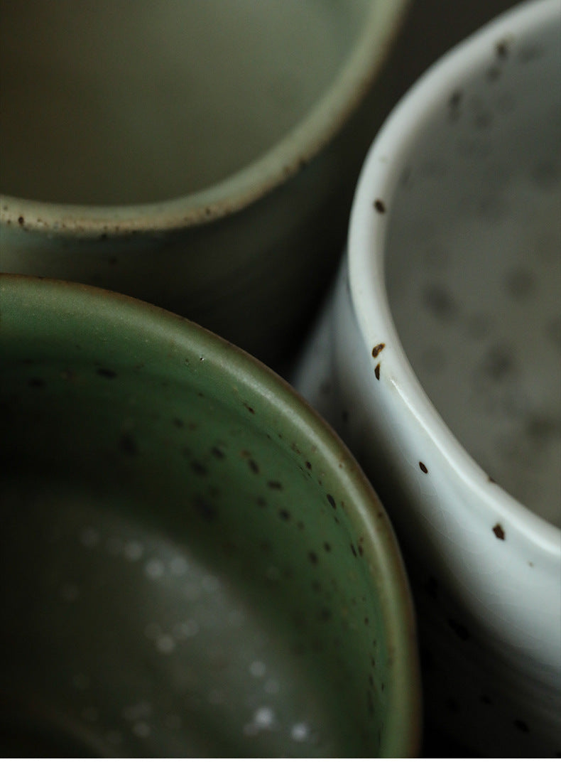 Close-up of three ceramic Matcha bowls with speckled glaze in green, white, and beige.