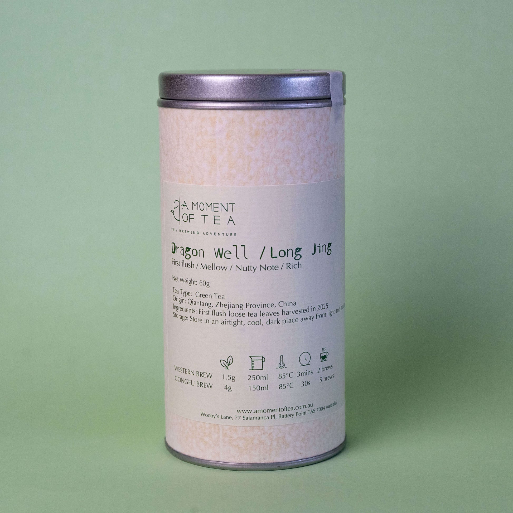 A canister of Dragon Well (Long Jing) green tea with a clear lid, next to a transparent bowl filled with flat, green tea leaves.