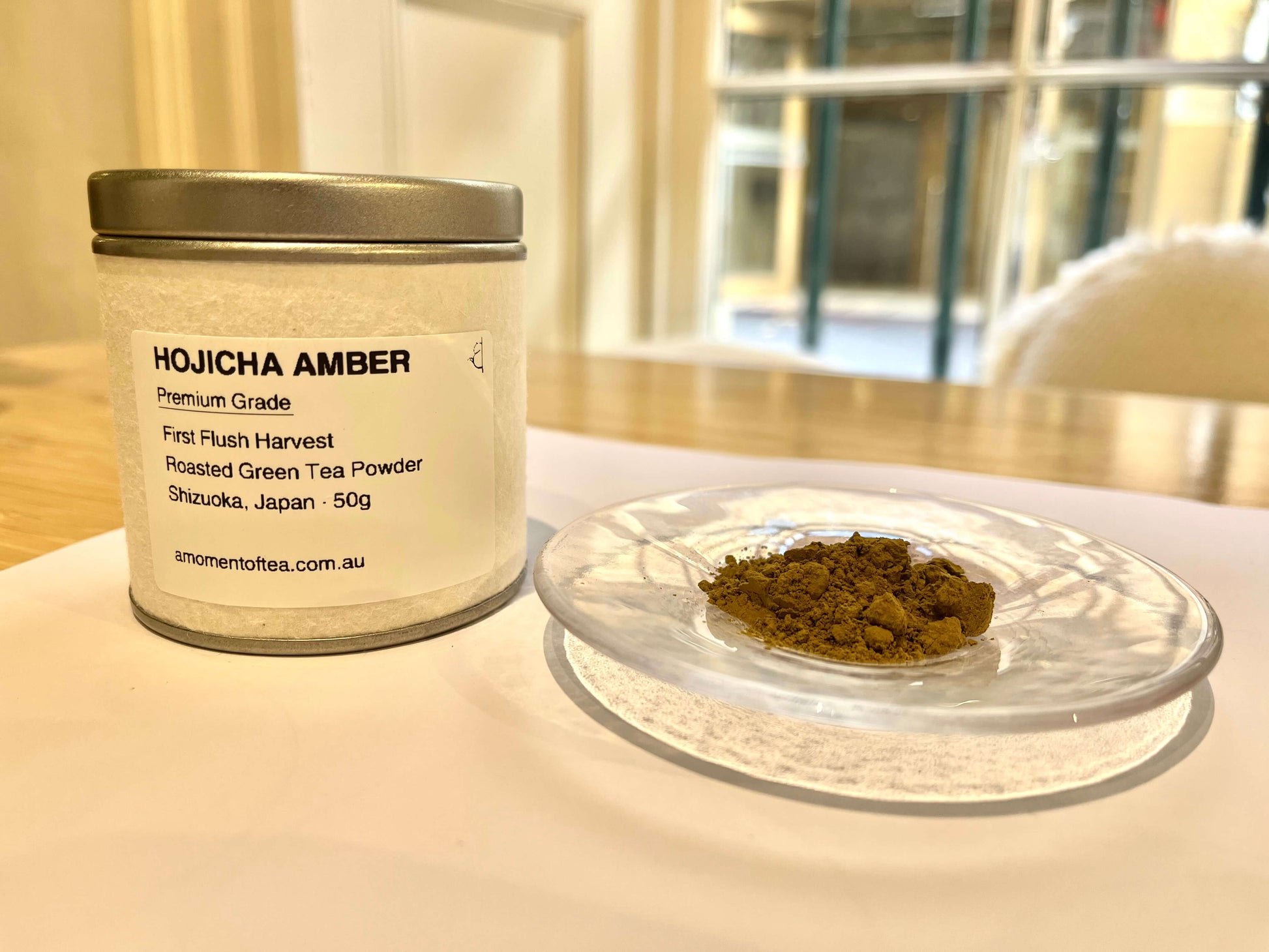 Hojicha Powder Amber tin with roasted green tea powder on a glass plate