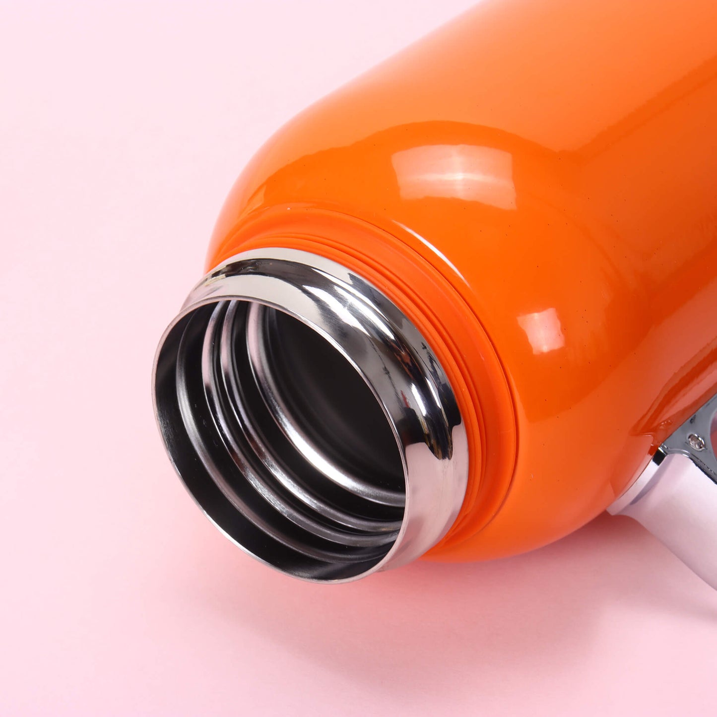Close-up of an orange thermos with a silver interior on a pink background