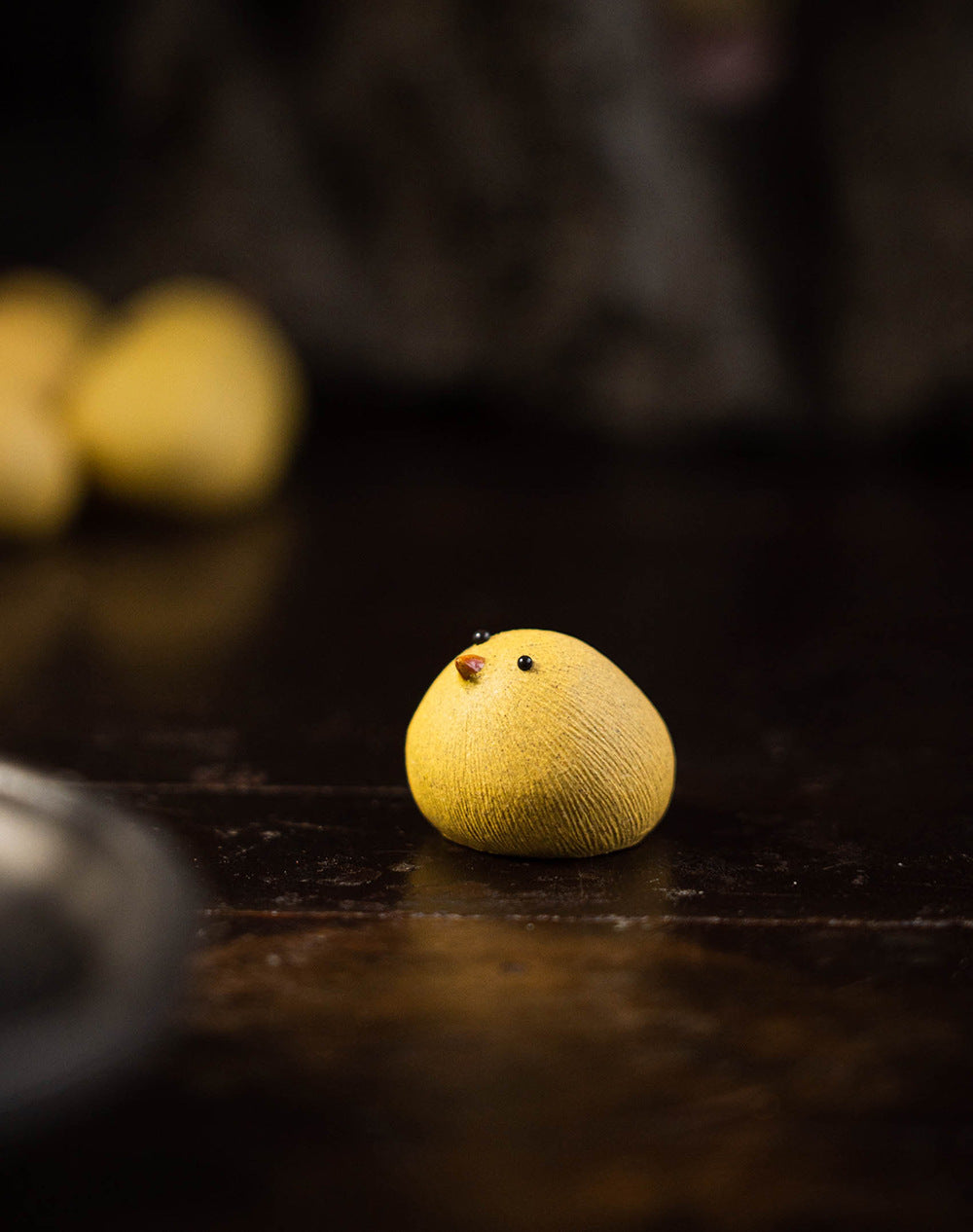 Small yellow bird figurine on a dark surface with blurred background