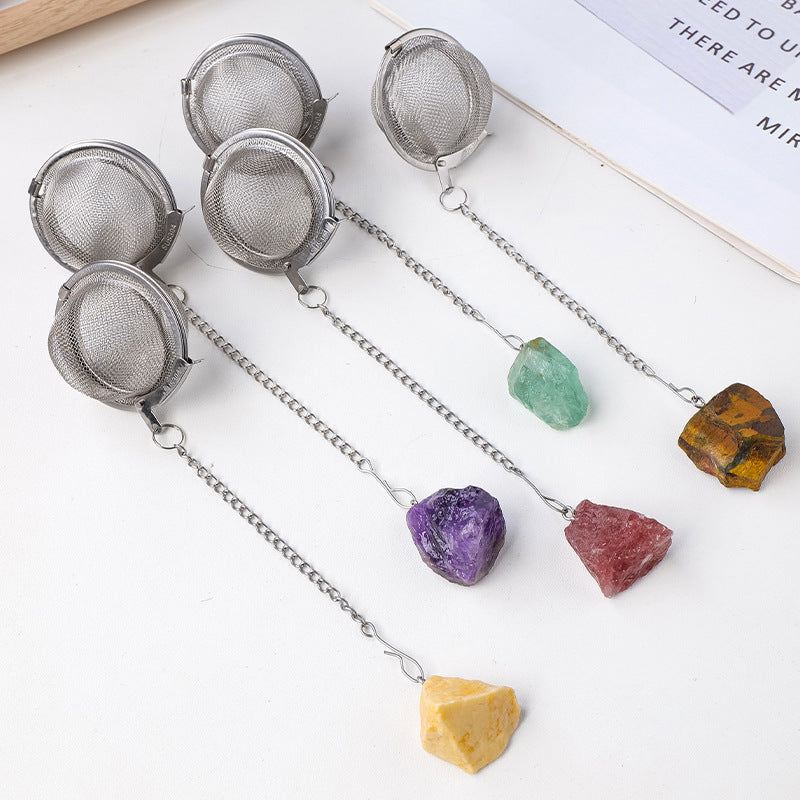 Five mesh tea infuser balls on a book, each with a different raw crystal stone on the chain