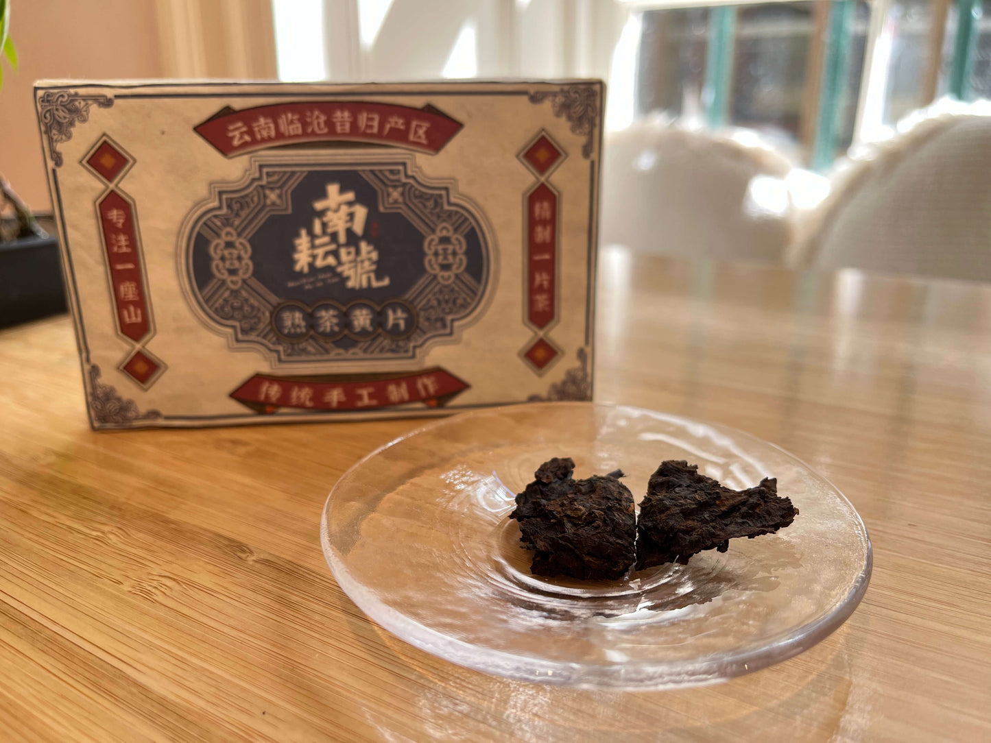 Ripe puer Tea cake on a clear stand with a branded box in the background