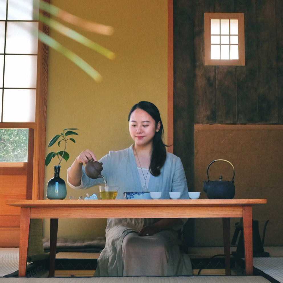 Woman sitting at a wooden table pouring tea