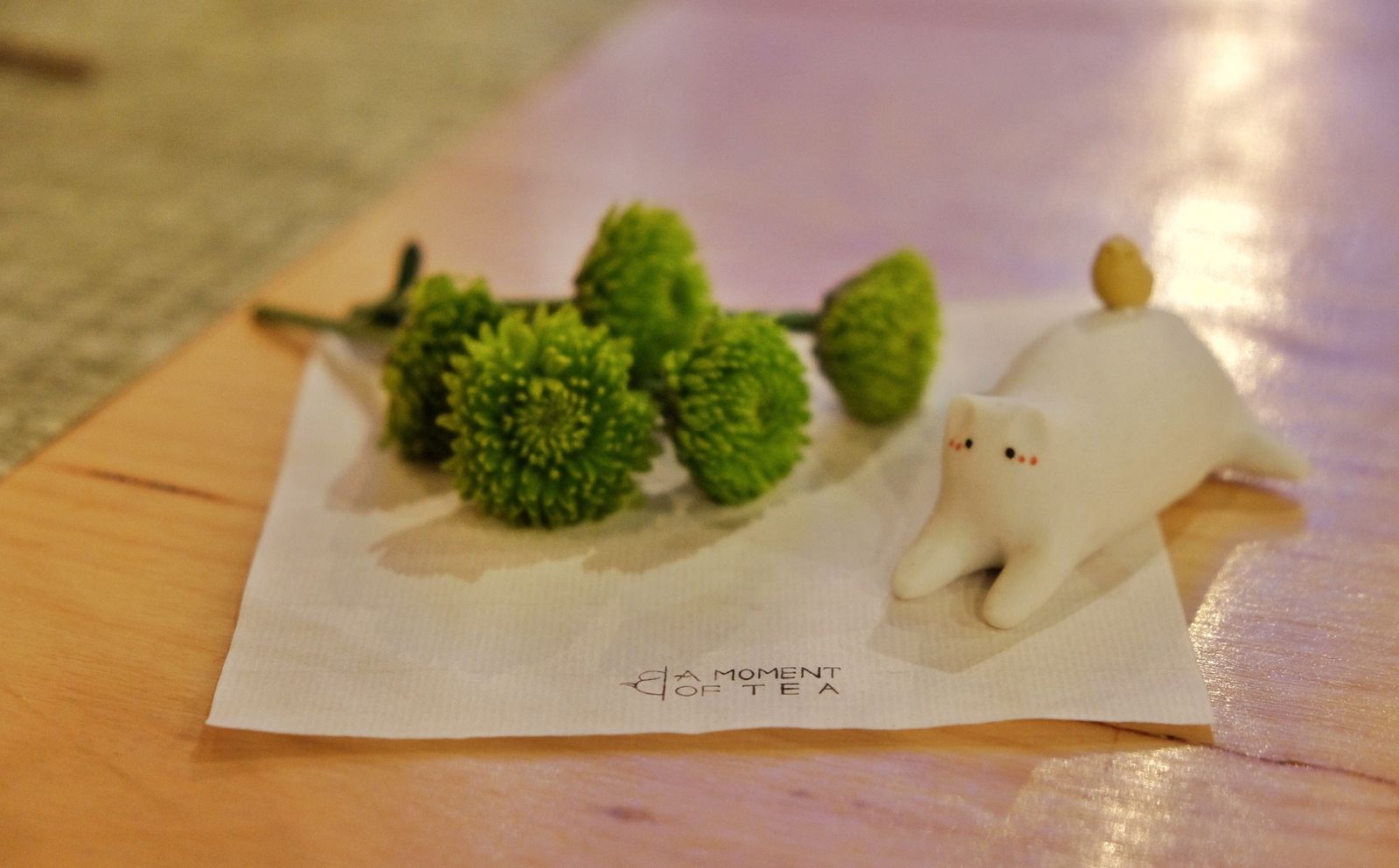 Cat tea pet on a branded napkin beside chrysanthemums