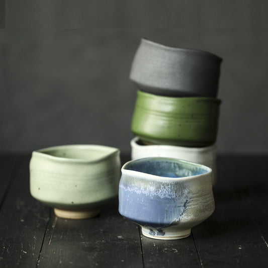 Collection of ceramic Matcha bowls in various colours on a dark wooden surface.
