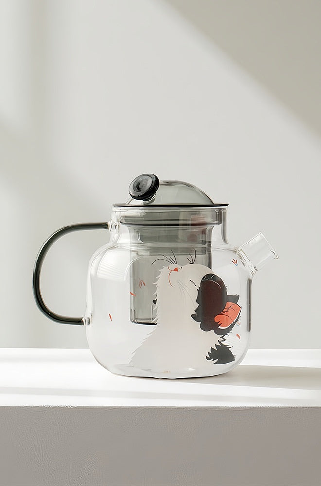Front view of the cat and butterfly glass teapot on a white surface, showing the smoke-grey glass infuser inside
