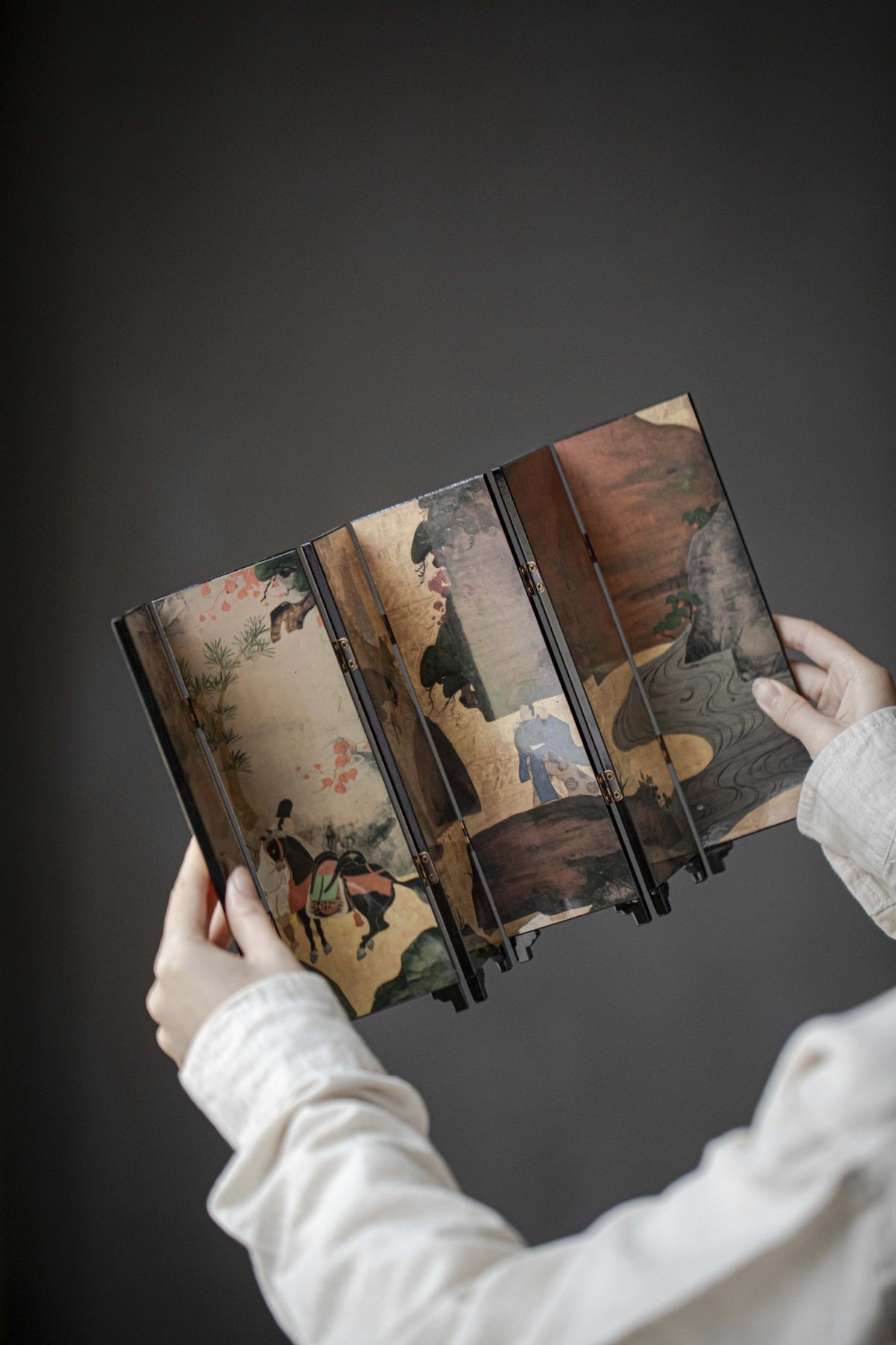 Gold Meadow mini folding screen, reverse: mountain scene with pines, a stream and a saddled horse, held in two hands
