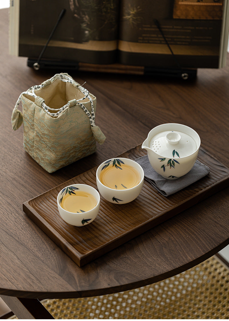 Tea set with cups and a teapot on a wooden tray, accompanied by a green fabric bag.