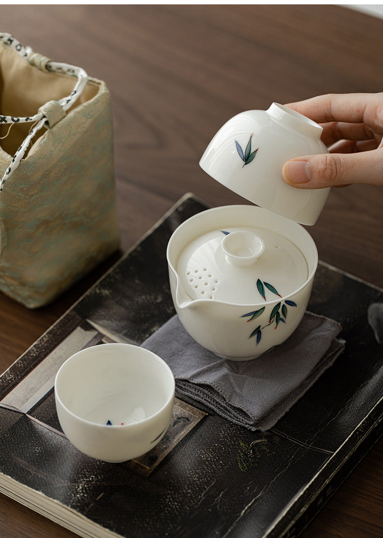White ceramic teapot and cup with green leaf design on a dark surface.