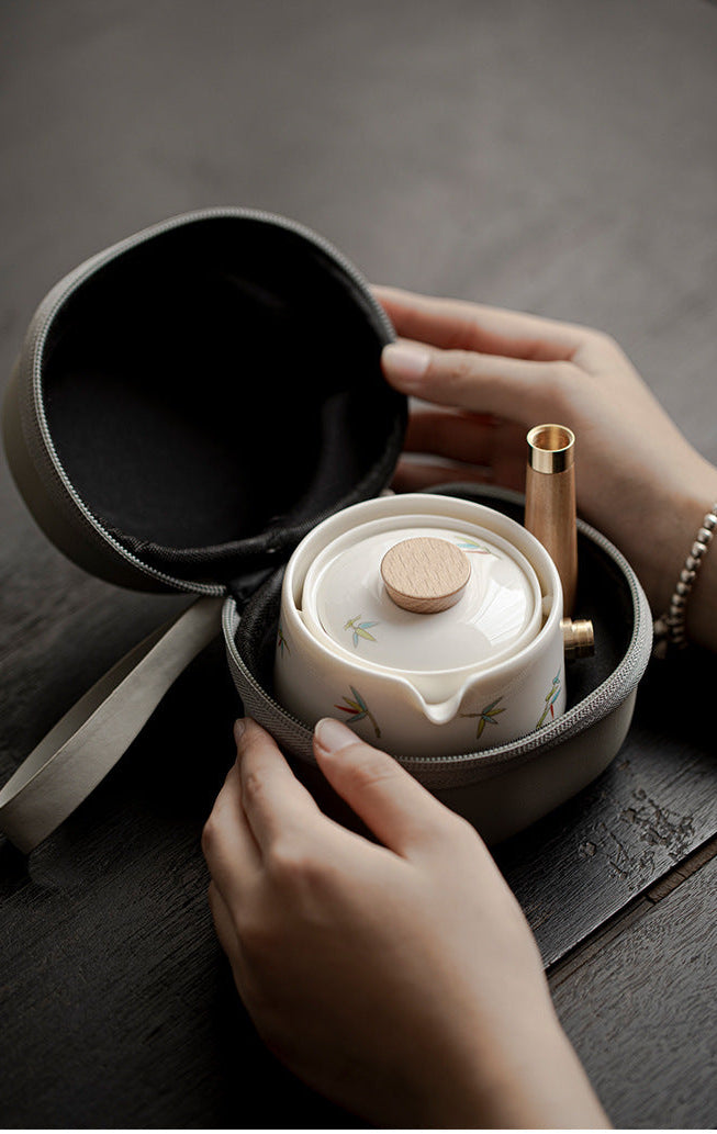 Person opening a compact travel tea set with a black lid and beige body on a dark surface.