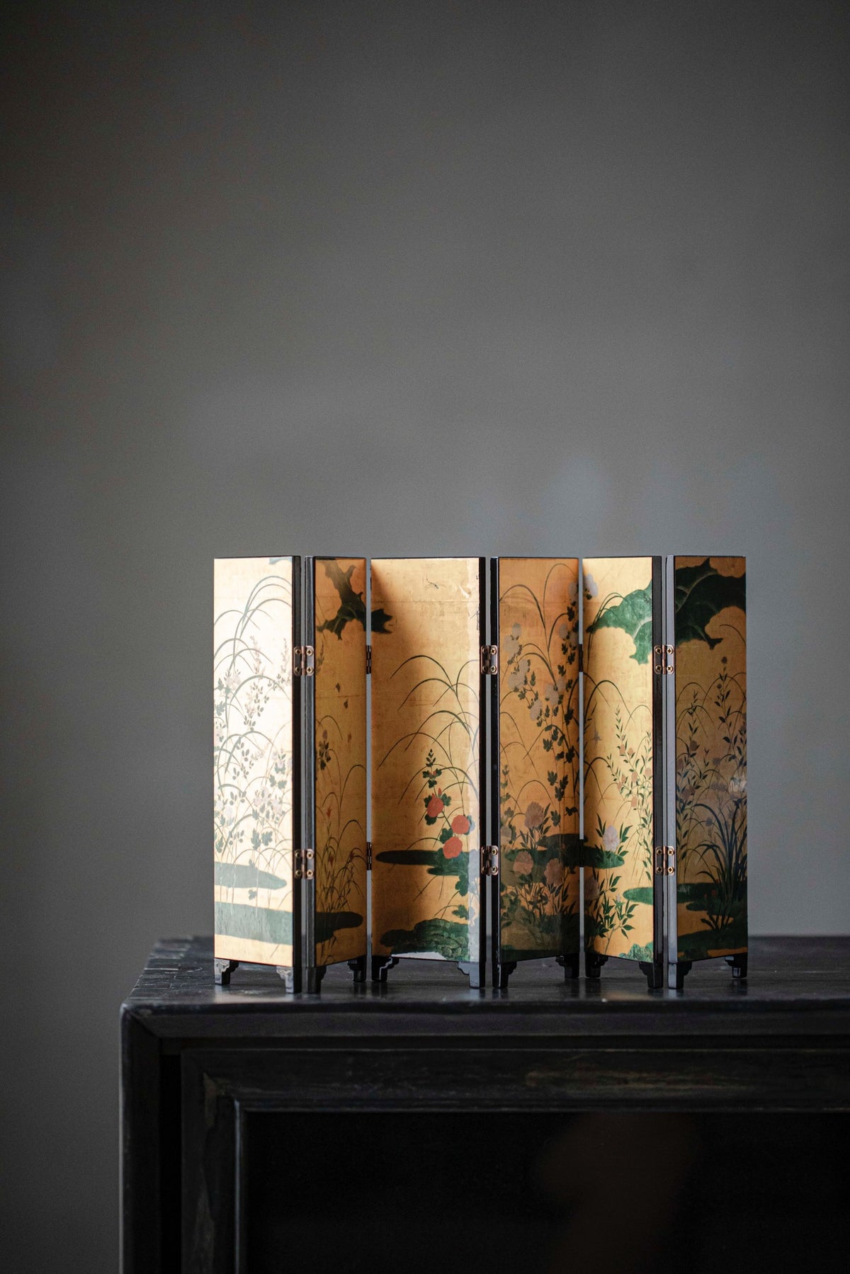 Gold Meadow mini folding screen, front: autumn grasses and wildflowers on a gold ground, five panels standing on a black cabinet