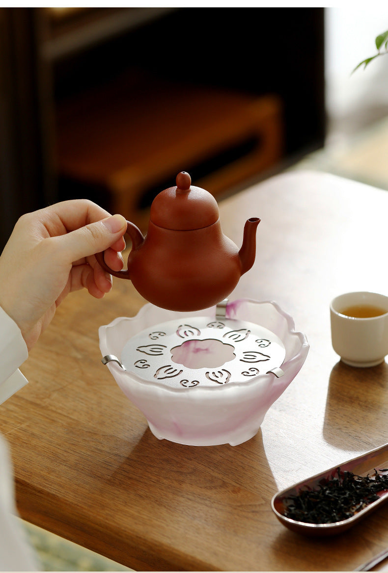 Small clay teapot being placed on the pink glass tea warmer