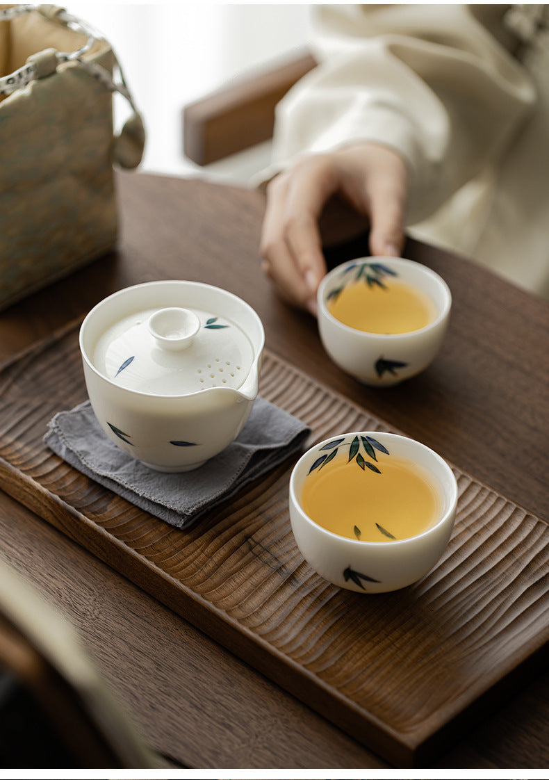 Three white ceramic tea cups with green leaf design on a wooden tray.