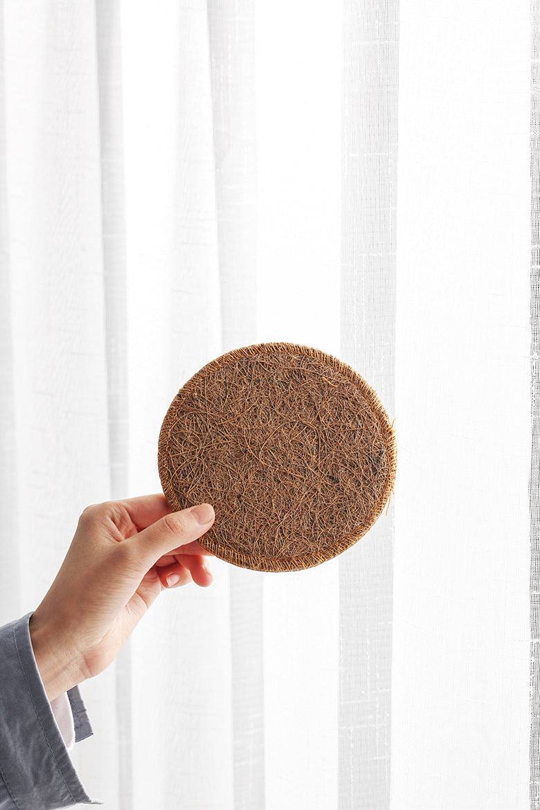 Loofah coaster held up against a white curtain