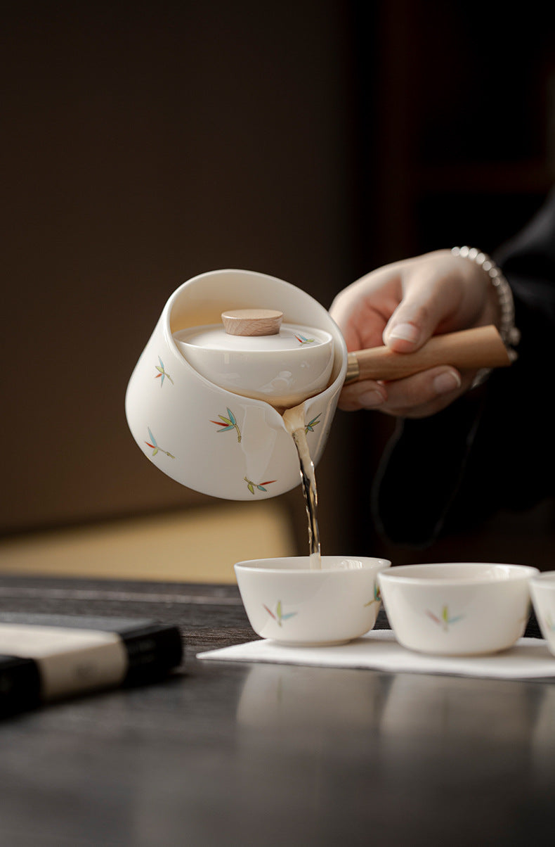 Tea being poured from a white teapot with floral designs into small white cups on a dark surface.