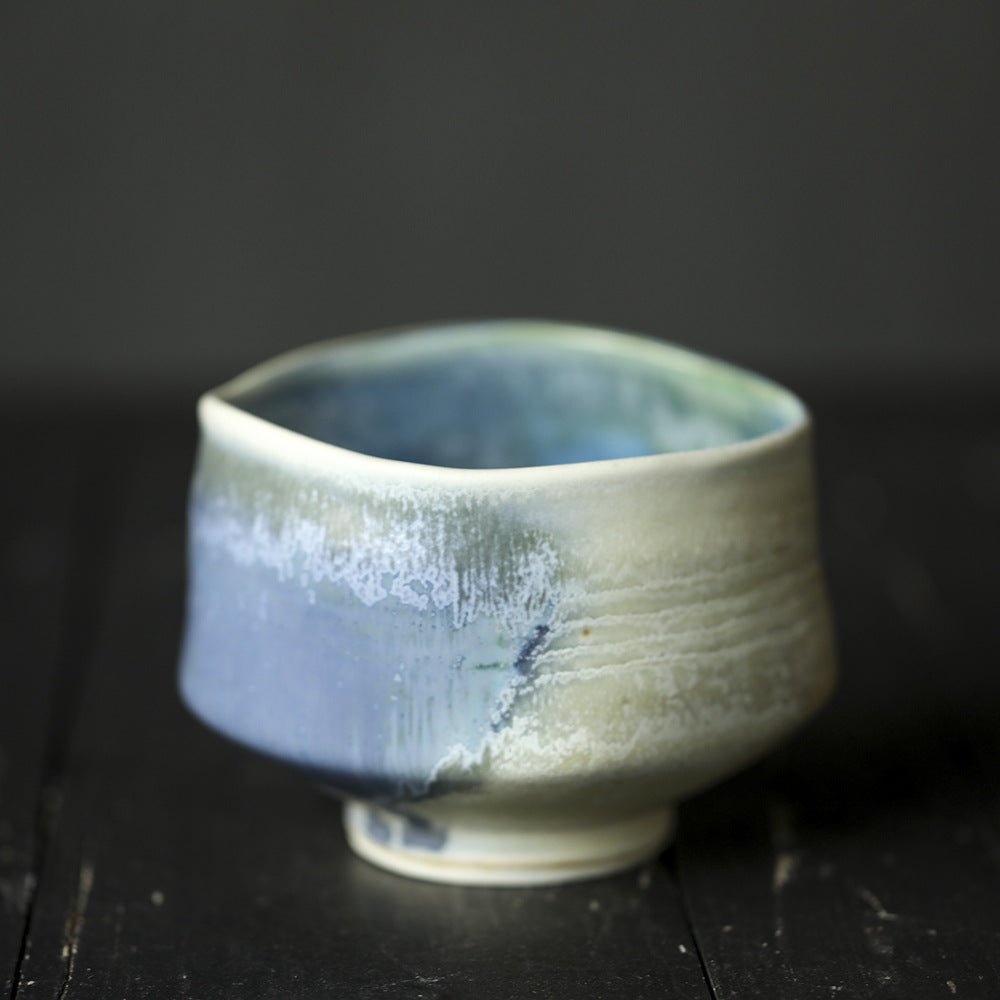 Ceramic matcha bowl with blue and white glaze on a dark background