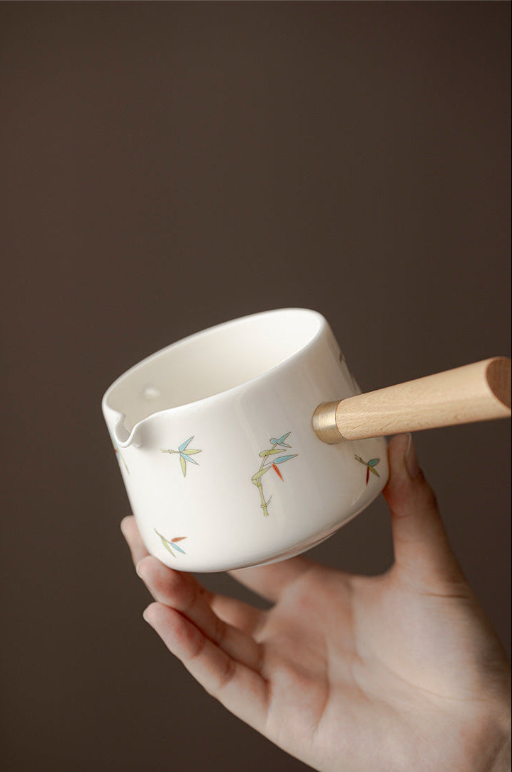White ceramic cup with wooden handle held by a hand against a brown background