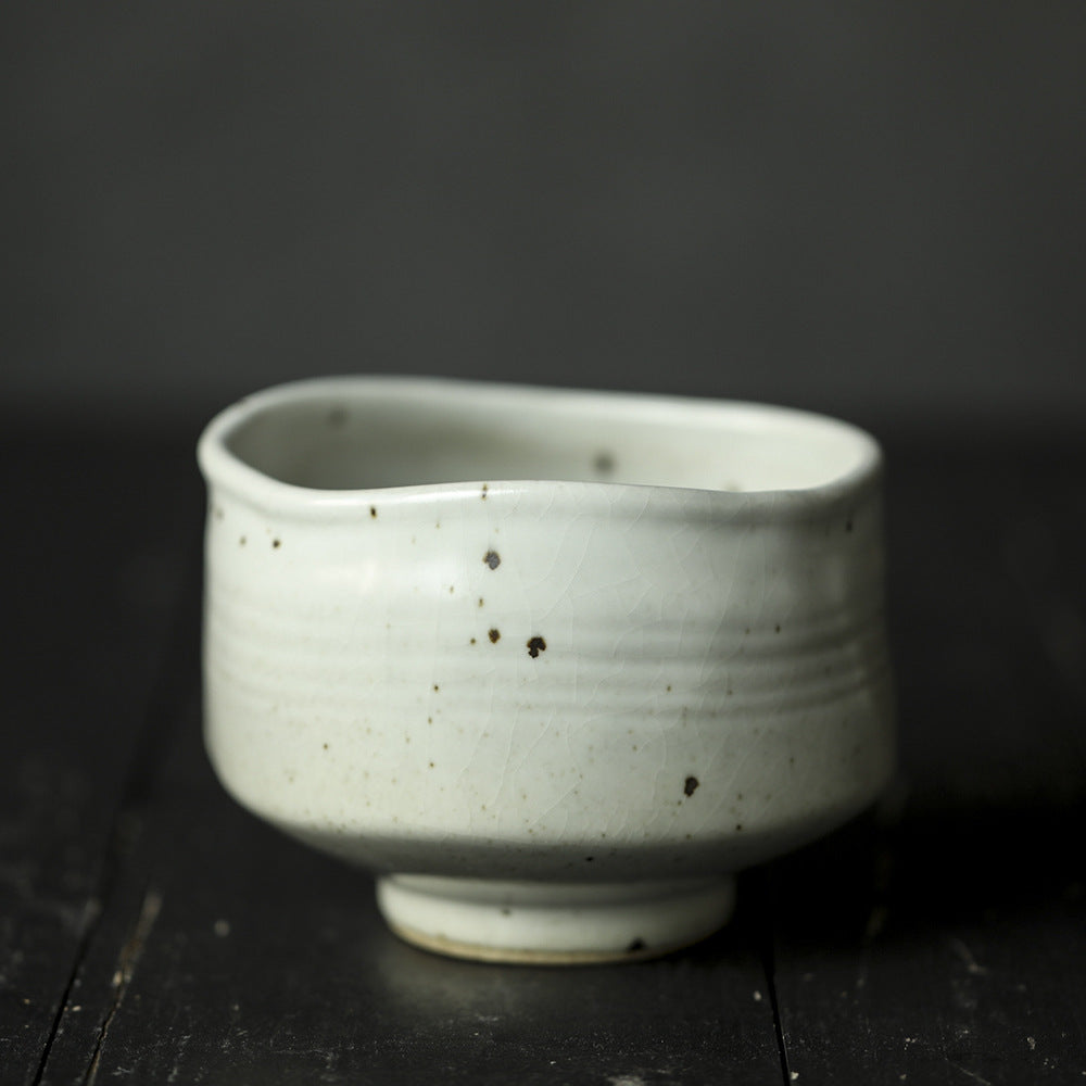 White ceramic Matcha Bowl with speckled texture on a dark wooden surface