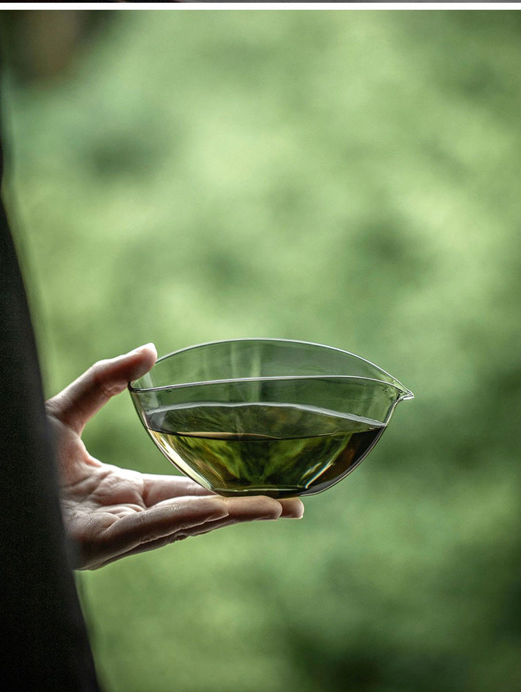 Hand holding smoked glass matcha bowl with tea by a window