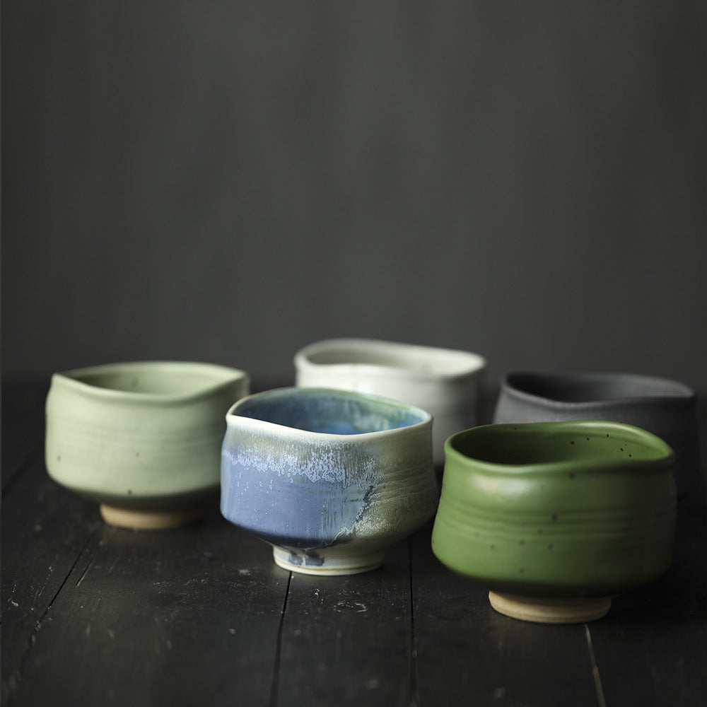 Set of ceramic Matcha Bowls in various colors on a dark wooden surface with a dark background
