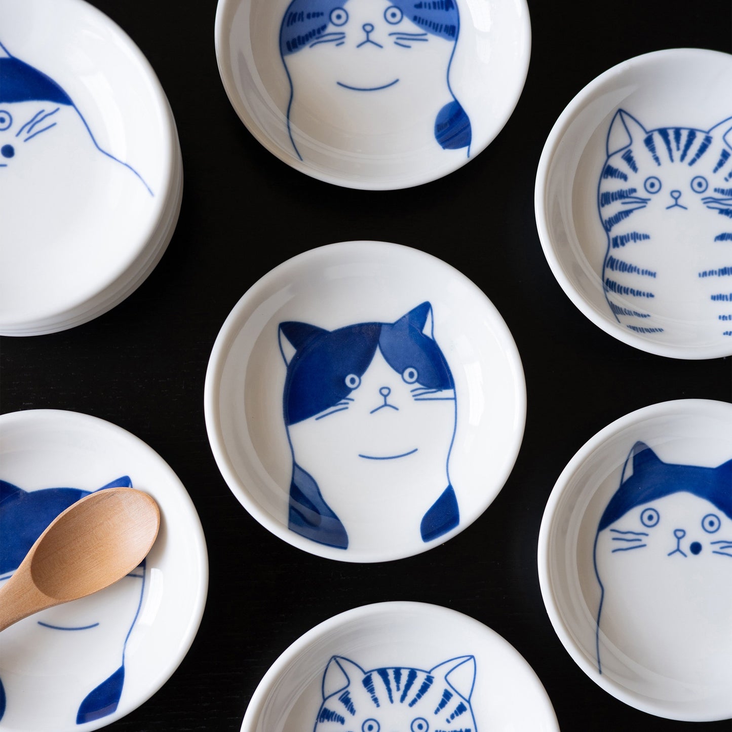 Blue cat face sauce dishes, all four cats on a black table with a wooden spoon