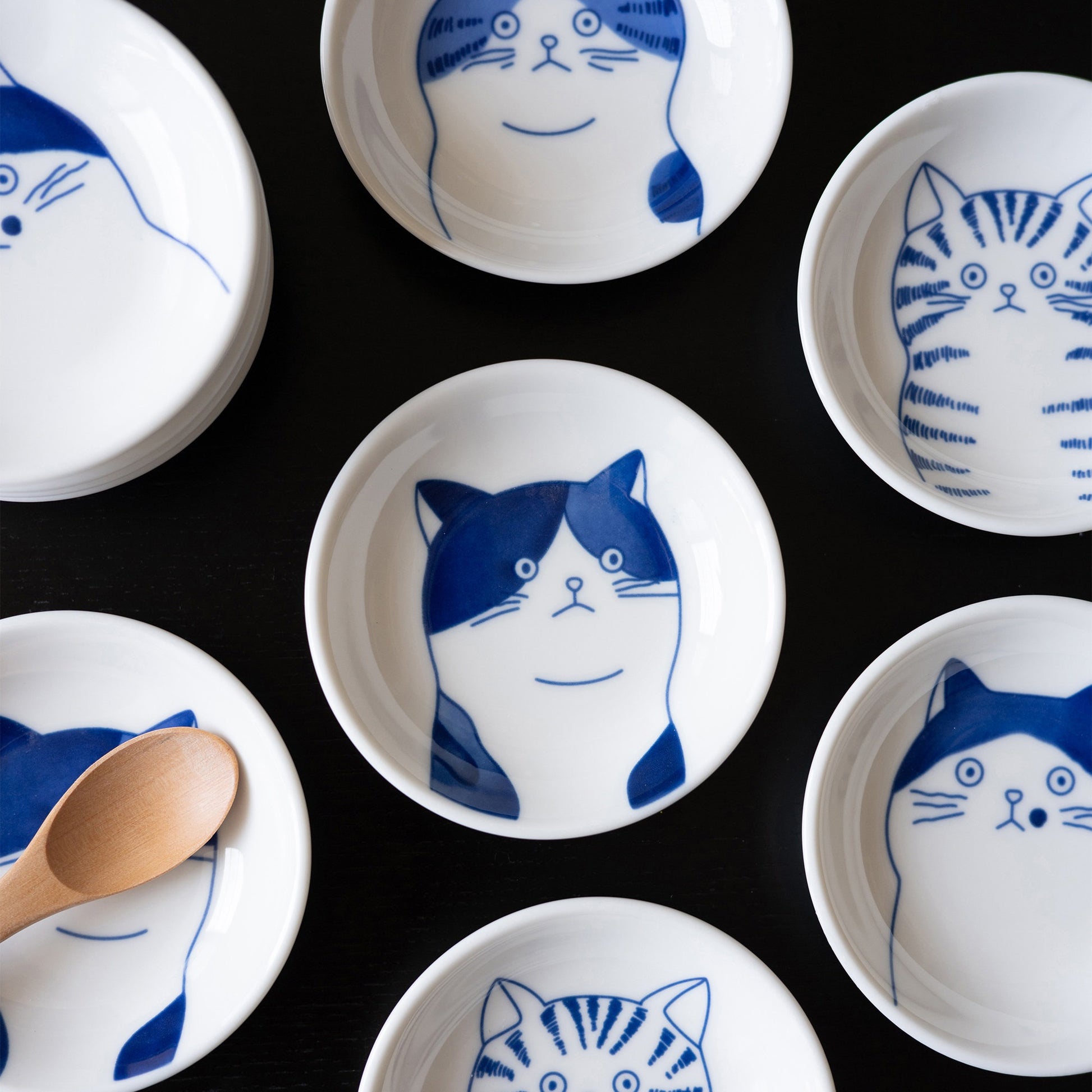 Blue cat face sauce dishes, all four cats on a black table with a wooden spoon