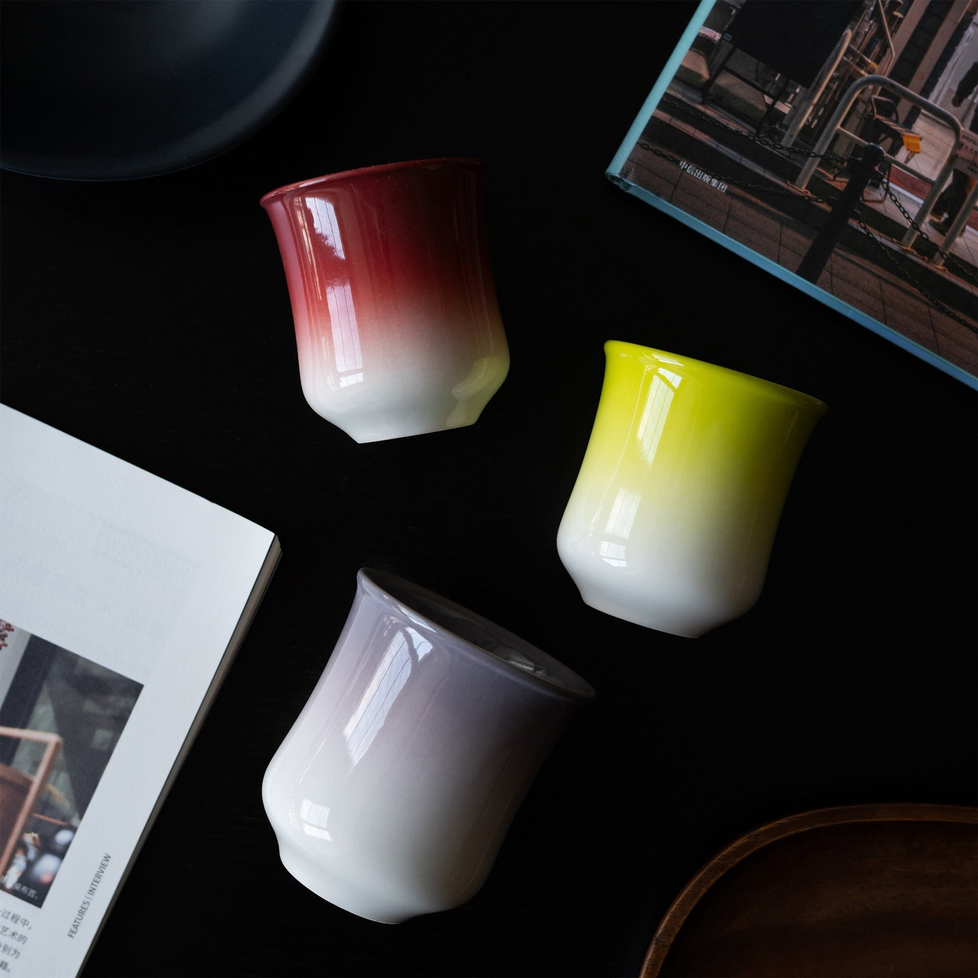 Gradient glaze tea cups on a black table with a magazine