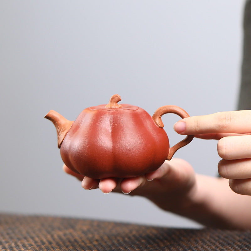 The Pumpkin Yixing clay teapot held in one palm, side on, showing its 180ml size against the hand