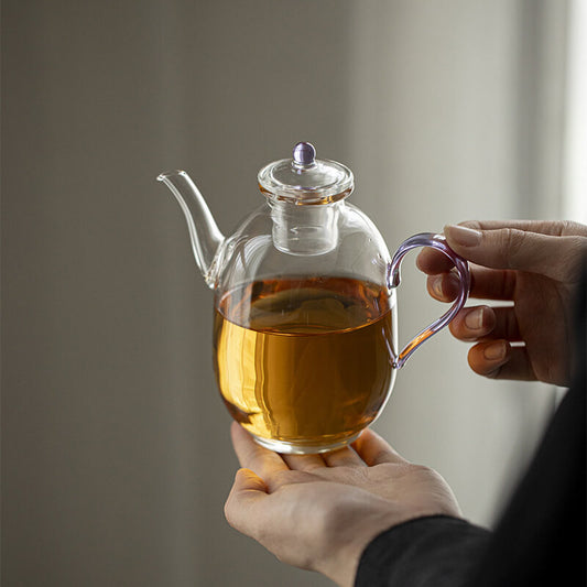 Glass teapot with tea held by a person against a neutral background
