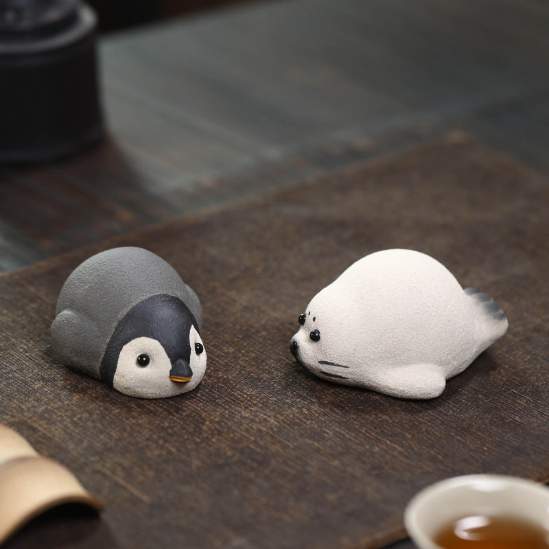 Penguin and seal Yixing clay tea pets side by side on a brown tea mat
